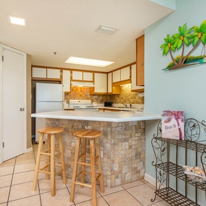 Inviting kitchen area features a breakfast bar with wooden stools, complemented by stone accents and tropical decor