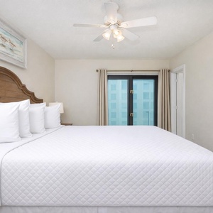 This bedroom features a plush king bed with crisp white linens and a serene view through large windows