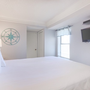 The bedroom features a comfortable bed, a mounted TV, and natural light from the window, perfect for relaxation