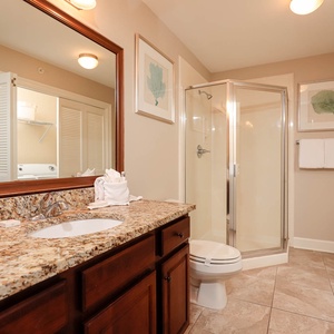The extra bath features a sleek granite countertop, a glass walk-in shower, and laundry area with a washer and dryer