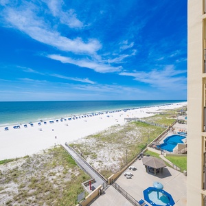 The view showcases a pristine beach with white sand and blue umbrellas, framed by a sunny sky and inviting turquoise waters