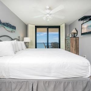 Unwind in the inviting master bedroom featuring a king bed, TV, and a view of the beach from the balcony