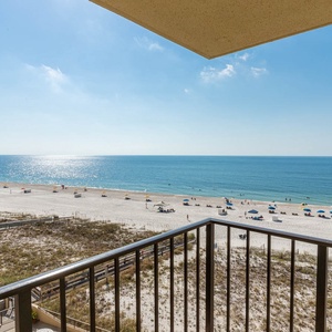 A spacious balcony offers a panoramic view of the tranquil beach and vibrant umbrellas dotting the white sand shoreline