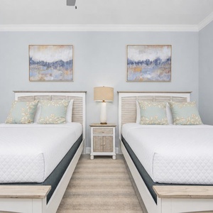 Relax in this guest bedroom featuring two comfortable queen beds, decorative pillows, and soothing artwork