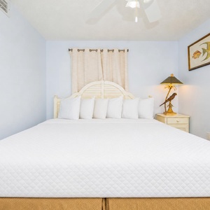 Brightly decorated guest bedroom featuring a king bed with white linens, complemented by coastal artwork and a stylish lamp