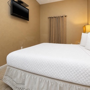 Guest bedroom featuring a queen bed, wall-mounted TV, and warm lighting from a bedside lamp, creating a relaxing atmosphere