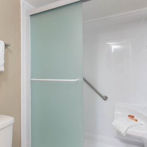 Walk-in shower with a frosted glass door, grab bar, and fresh towels in the master bath for a refreshing experience