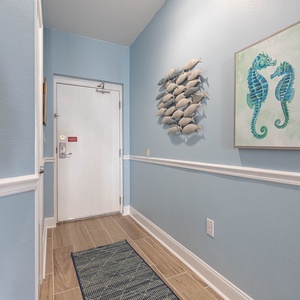 The entryway features soft blue walls, decorative fish art, and a welcoming rug, creating a bright and cheerful atmosphere