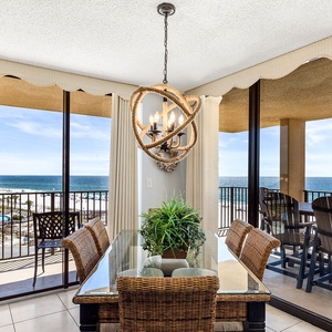 The dining area features a glass table with six chairs and offers a beautiful view of the beach from large sliding doors