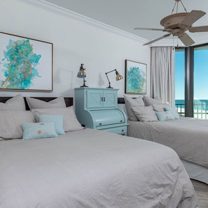 Relax in the tranquil guest room featuring two comfortable queen beds, coastal art, and large windows with beautiful views