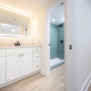 Luminous master bath featuring a sleek vanity with ample storage and a walk-in shower adorned with stylish teal tiles