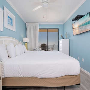 Serene master bedroom featuring a plush king bed with white linens, coastal artwork, and beach balcony access