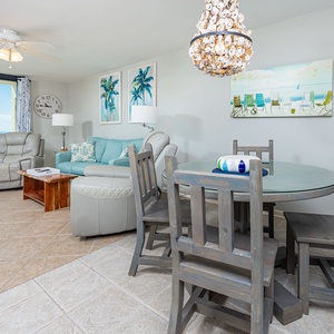 Living area features a light blue sofa with queen sleeper, a round dining table, and balcony offering views of the beach