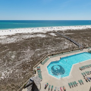 Expansive views of the beach stretch beyond the inviting pool area, showcasing white sand and vibrant blue waters