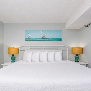 This inviting bedroom features a large bed with plush pillows, bright lamps, and artwork, creating a relaxing retreat