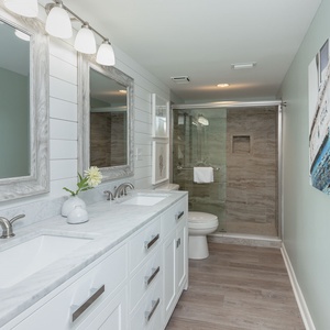 The master bath features a dual sink vanity with marbled countertops, a walk-in shower, and coastal artwork on the wall