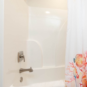 This bathroom features a clean, bright design with a colorful coral-themed shower curtain and a spacious tub for relaxation