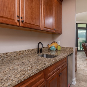 This wet bar features rich wooden cabinetry, a sleek granite countertop, and a cozy view of the inviting living area