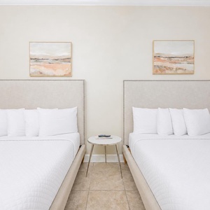 Rest comfortably in this guest bedroom featuring two queen beds, soft linens, and serene coastal artwork above