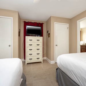 The guest bedroom features two queen beds, a dresser with TV, and an adjoining bathroom with fresh towels on the counter
