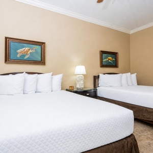 This guest bedroom features two comfortable queen beds, charming turtle artwork, and a bedside lamp for a cozy ambiance