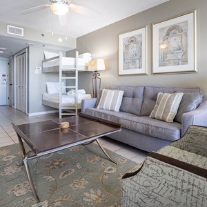 A cozy living area features a gray sofa with queen sleeper, decorative armchair, and twin bunk beds against a light wall