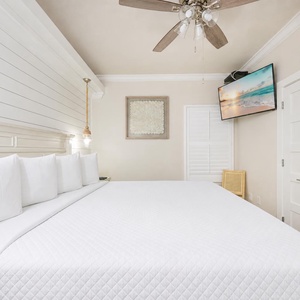 A cozy bedroom features a king bed adorned with decorative pillows, a mounted TV, and soft lighting