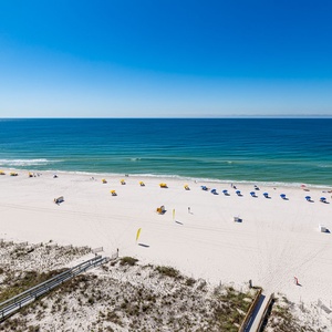 A serene beach view showcases vibrant blue umbrellas lining the shore, inviting guests to relax on the white sand
