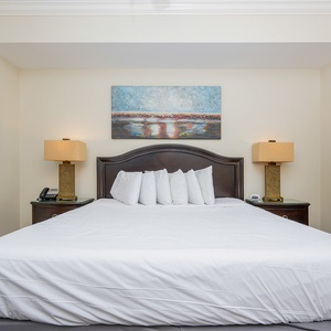 The master bedroom features a large king bed, plush pillows, warm lighting, and colorful artwork, creating a relaxing retreat