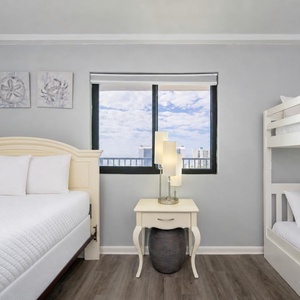 Guest suite offers cozy twin bunks and a queen bed beside a window with clouds drifting in blue skies
