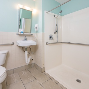 This accessible bathroom features a roll-in shower, bathroom and shower rails, and a shower chair for safety and comfort