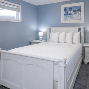 The master bedroom features a cozy queen bed with plush pillows, soft blue walls, and a serene atmosphere perfect for relaxation