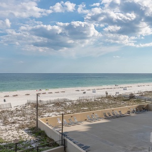 The view showcases a serene beach front with white sand and turquoise waters, framed by the poolside area with lounge chairs