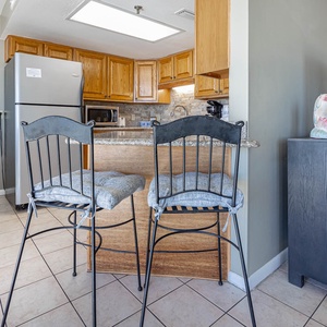 The kitchen area features wooden cabinets, a granite countertop, and two high-top chairs, creating a welcoming space