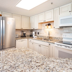 Brightly lit kitchen featuring granite countertops, a sleek refrigerator, and a cozy breakfast bar with seating