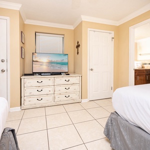 Guest bedroom featuring two double beds, a TV on a dresser, and a doorway leading to a bathroom with a modern vanity