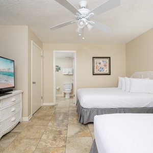 Guest bedroom featuring two double beds, a large TV, and an en-suite bathroom, with decorative accents and a ceiling fan