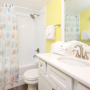 Brightly colored guest bathroom featuring a tub/shower combo, fresh towels, and a decorative sea turtle accent on the wall