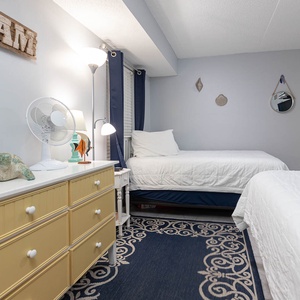 The guest bedroom features two comfortable beds, a charming dresser, and beach-themed decor for a relaxed getaway