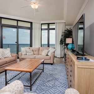 This living area features a large TV, cozy seating, and stunning beachfront views through expansive windows