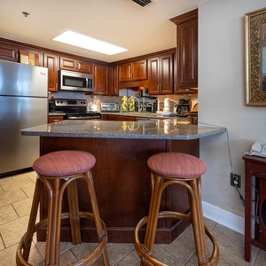 Rich wooden cabinetry complements the granite countertops in this modern kitchen with a breakfast bar and two stools