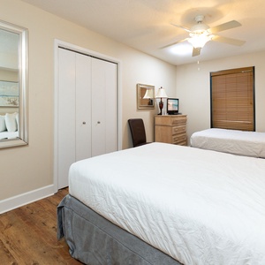 This guest bedroom features two neatly made full beds, a bedside table with a lamp, and coastal-themed artwork on the walls