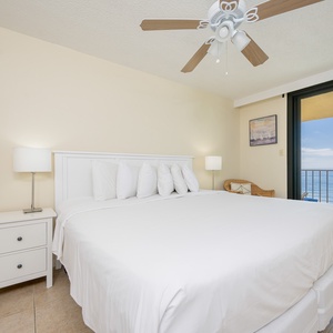 Bright master bedroom featuring a king bed, bedside lamp, and the balcony with seating overlooking the tranquil beachfront