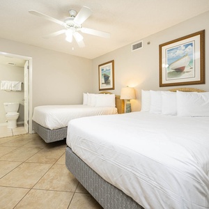 Guest bedroom featuring two double beds, soft white linens, a ceiling fan, and coastal artwork for a relaxing atmosphere