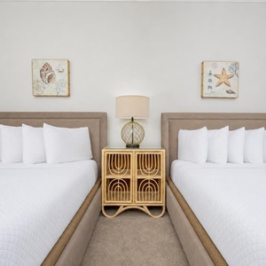 Guest bedroom featuring two queen beds, decorative coastal art, and a stylish lamp on a stylish nightstand