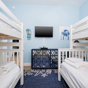 Bunk room with a twin bunk and a twin over double bunk with a trundle, TV, and coastal decor, creating a fun space for kids