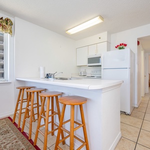 This kitchen features a bright, clean design with white cabinetry, a breakfast bar with wooden stools, and modern appliances