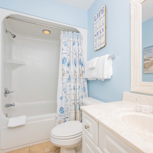 Bright guest bathroom featuring a tub/shower combo, elegant vanity, and beach-themed decor for a refreshing retreat