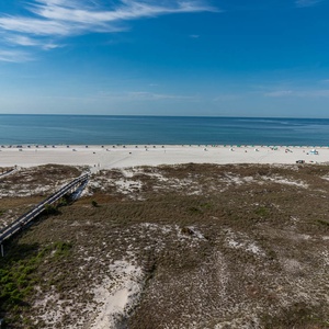 Expansive view of the beach with white sand, beach chairs, and a wooden walkway leading to the shimmering gulf waters