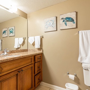 Enjoy the guest bathroom featuring a large granite countertop, stylish decor, and vibrant coastal artwork